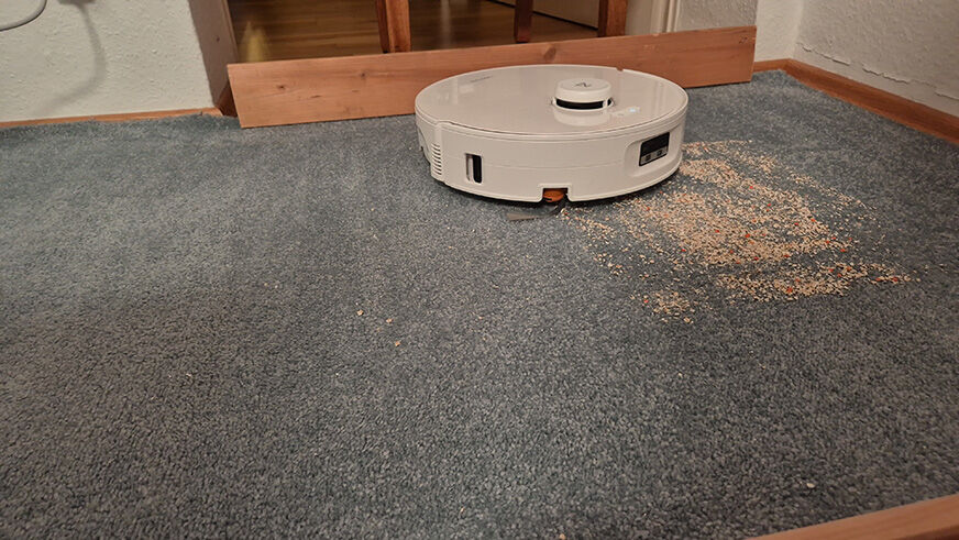 Der Roborock Qrevo Curv 2 Flow reinigt einen Teppich mit Haferflocken und Sand.